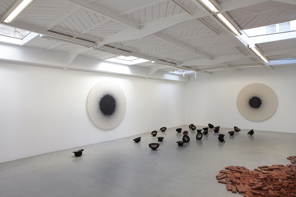 Latifa Echakhch – Tkaf, 2011 / Installation in situ : Briques et pigment. Dimensions variables. / – Mer d’encre, 2012 Installation au sol. Chapeaux melon, résine et encre. Dimensions variables / – Tambour 36′ & Tambour 93′, 2012 / Encre indienne noire sur toiles. 173 cm de diamètre / Vue de l’exposition « Tkaf », kamel mennour, Paris, 2012 / © Latifa Echakhch Photo. Fabrice Seixas / Courtesy the artist and kamel mennour, Paris